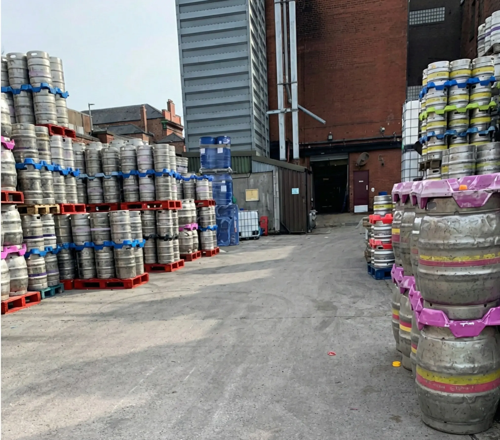 Brewery yard at Joseph Holt showing stacked beer kegs with coloured handles ready for distribution to pubs across Manchester